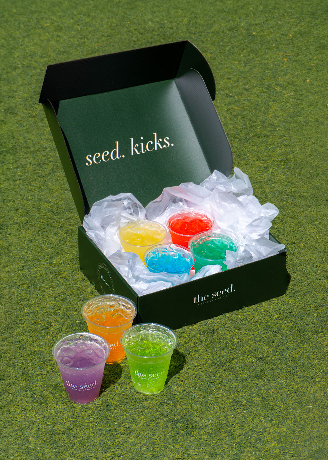Colorful low sugar plant based energy drink in clear cups with a 'seed. kicks.' box on a green background